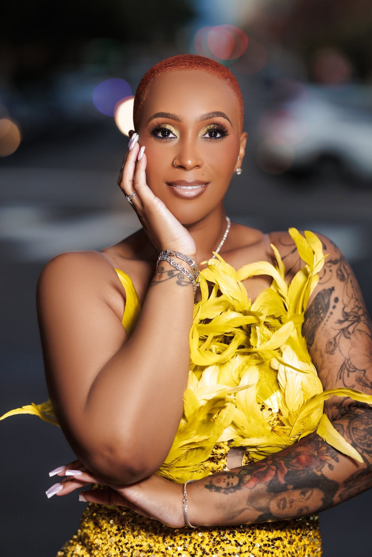Jamie Gainey in a yellow feathered top, hand resting on her cheek
